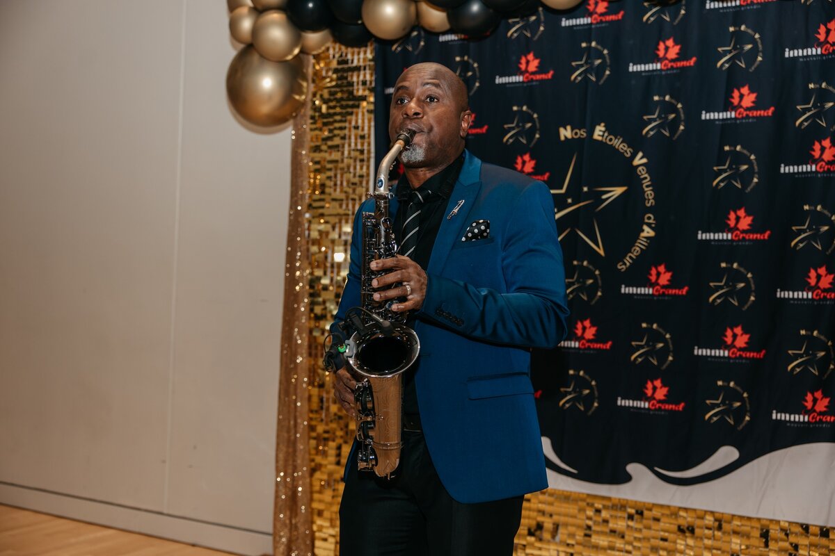 Saxophoniste sur scène devant la bannière N.É.V.A.